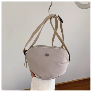 Close-up of beige shell bag with metal interlocking logo and wide canvas strap
