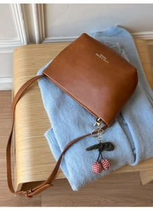 Close-up of brown leather bucket bag with a red checkered cherry charm on blue cardigan