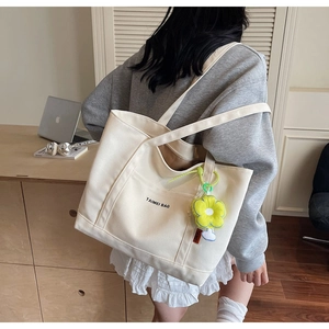Dettaglio borsa tote in tela crema con scritte nere e ciondolo a forma di fiore giallo