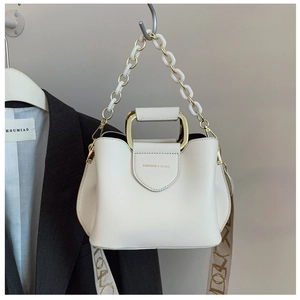 Detail of white bucket bag with gold handle and embroidered wide shoulder strap