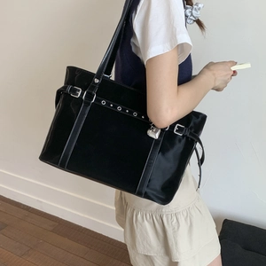 Detail of black glossy tote bag with silver heart charm and metal eyelet straps