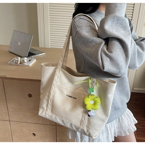 Dettaglio della borsa tote in tela crema con ciondolo a fiore giallo e tasca