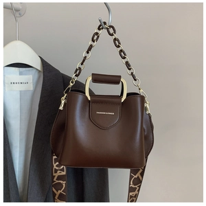 Detail of dark brown leather bucket bag with gold metal handle and patterned strap