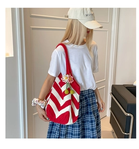 Detail of red and white striped hand-knitted shoulder bag with a daisy charm accessory