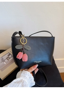 Close-up of black leather crossbody bag featuring a decorative red cherry charm and logo