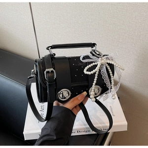 Détail du sac cylindrique noir à pois avec nœud en dentelle blanche et perles décoratives