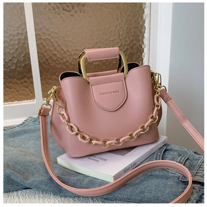 Pink matte leather bucket bag featuring gold metal handle and decorative chain detail