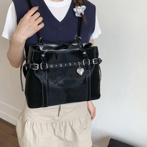 Close-up of black patent leather tote bag with silver heart charm and metal buckles
