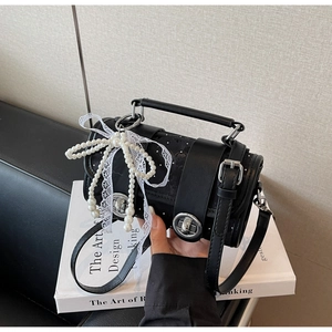 Détail d'un sac cylindrique noir avec un nœud en perles et un ruban en dentelle
