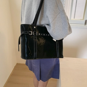 Side view of black glossy tote bag with decorative silver buckle and rivets on shoulder strap