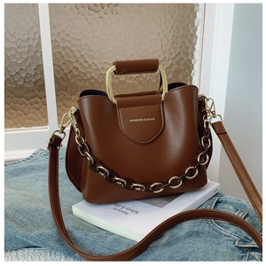 Close-up of brown textured leather bucket bag with metal U-shaped handle and chain detail