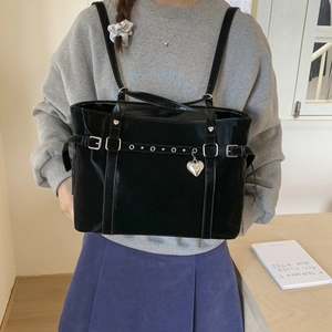 Detail of black patent leather tote bag featuring silver eyelets and a heart pendant