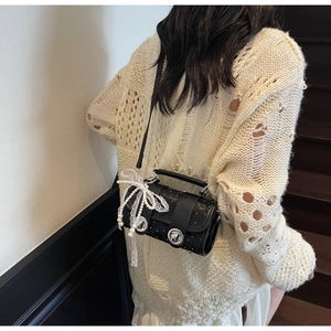 Détail du sac bandoulière cylindrique noir avec boucles argentées et nœud en dentelle