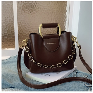 Detail of dark brown bucket bag with gold U-shaped handle and metal chain on denim fabric