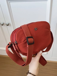 Brick red nylon crossbody bag with three zipper compartments and wide shoulder strap
