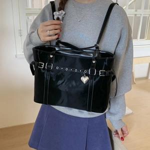 Detail of black patent leather tote bag with silver heart pendant and metal stud straps