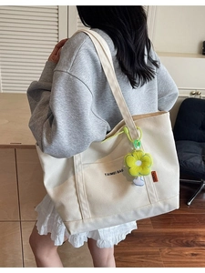 Borsa tote in tela crema minimalista con scritte nere e ciondolo a fiore giallo