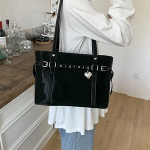 Detail showing shiny black tote bag with silver hardware and heart charm in a lifestyle setting
