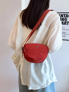 Red textured fabric crossbody bag with silver DD logo shown on a model in a minimalist setting