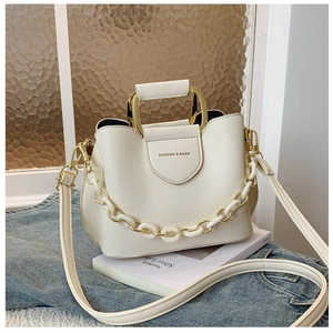 Detail of white structured handbag with gold U-handle, chain, and black interior lining