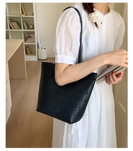 Detail of laser-cut hollow pattern and embossed logo on black faux leather tote bag