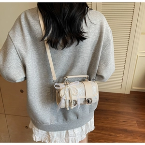 Détail d'un sac cylindre vintage crème avec dentelle et nœud en perles porté par un modèle