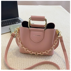 Detailed view of pink crossbody bucket bag with gold U-shaped metal handle and chain link