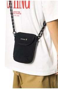 Detail of black crossbody phone bag featuring a branded flap and woven drawstring strap
