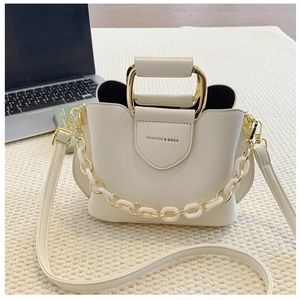 Detail of cream crossbody bucket bag featuring gold metal handle and decorative chain strap