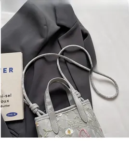 Détail de la broderie florale sur un sac cabas gris clair avec doubles poignées