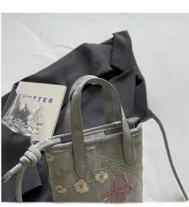 Détails des broderies florales et papillon sur un sac fourre-tout gris texturé