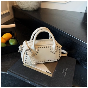 Detail of cream white crossbody bag with silver studs on black book background