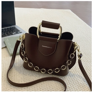Detail of a dark brown leather bucket bag with a gold metal handle and chain on a white rug