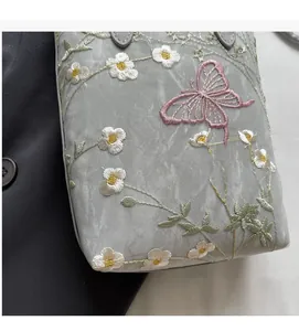 Détail d'une délicate broderie florale blanche avec papillon rose sur un cabas gris soyeux