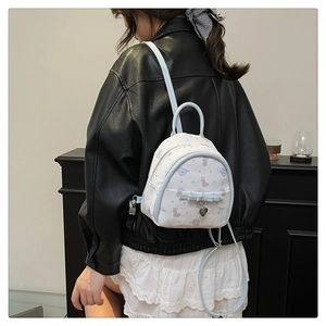 Gros plan d'un mini sac à dos avec imprimés cartoon, nœud bleu et breloque en cœur