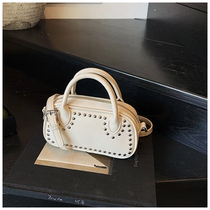 Detail of cream white mini barrel bag with silver studs on black book background