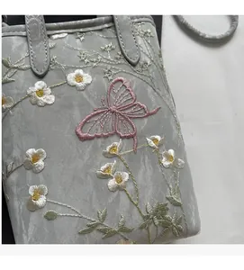 Broderie détaillée de fleurs et papillons sur un sac à bandoulière en soie grise