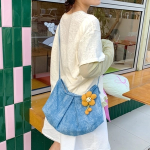 Détail du sac croissant en denim plissé bleu clair avec un porte-clés tournesol au café