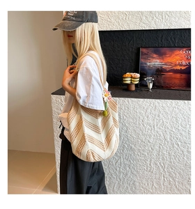 Close-up of woven shoulder bag featuring V-shaped stripes and a daisy pendant