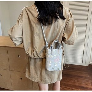 Gros plan détaillé d'un sac bandoulière bleu avec broderie de papillon rose
