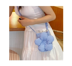 Dettaglio di una borsa a tracolla a fiori a scacchi blu indossata su un abito bianco