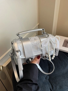 Sac cylindrique argenté avec nœud en dentelle blanche et breloques perles sur fond noir