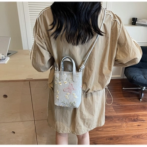 Détail de la broderie de fleurs et papillons sur un mini sac cabas bleu clair pour femme