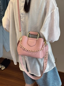 Pink leather bucket bag with gold handle and patterned strap shown on a model