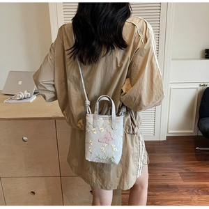 Détail du sac fourre-tout gris clair avec broderie de papillon rose et fleurs jaunes