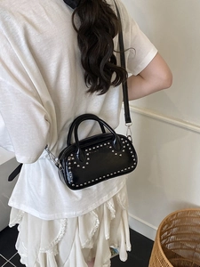 Black patent leather crossbody bag with silver studs worn by a model for size perspective