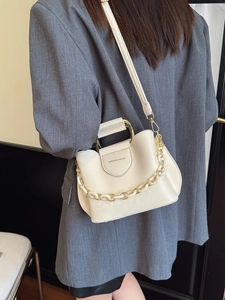 Creamy white bucket bag with resin chain and top handle worn by a model in a suit