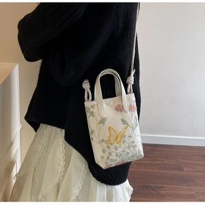 Gros plan du sac en toile blanche avec broderies de papillon jaune et de fleurs