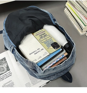 Top view of large blue denim backpack showing spacious interior with books and gadgets