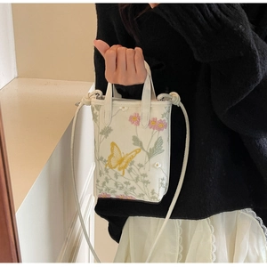 Détail montrant la broderie délicate de papillon jaune sur le sac cabas blanc crème